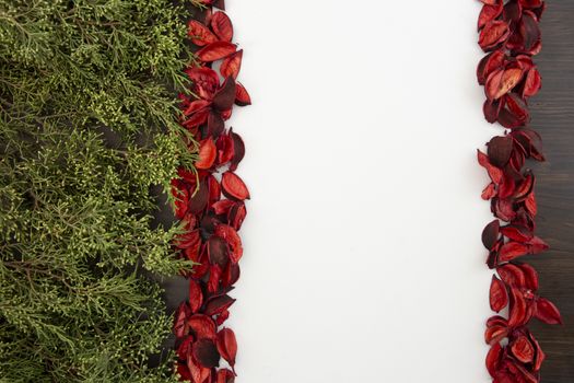 Flat lay Christmas copy space with pine branches on one side and red petals bordering a white background