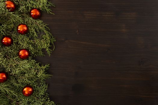 Flat lay Christmas copy space with pine branches and red Christmas baubles on a side on a dark wooden background