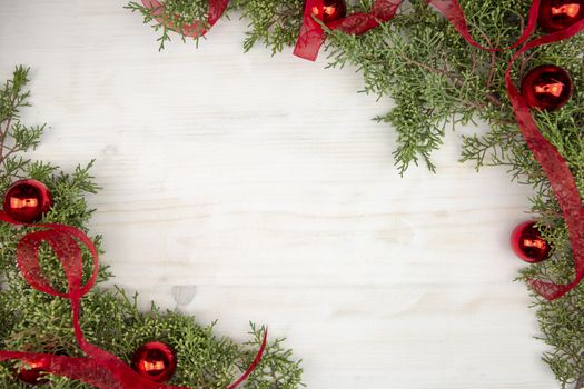 Flat lay Christmas copy space with pine branches, red organza ribbon and red Christmas baubles on a light wooden background