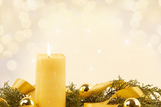 Christmas copy space with a lit yellow candle, pine branches, golden satin ribbon and gold-colored Christmas balls on a light patterned background