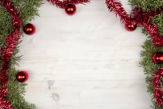 Flat lay Christmas copy space with pine branches, red garland and red Christmas baubles on a light wooden background