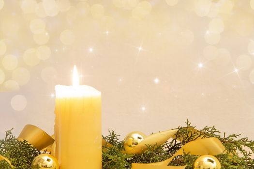 Christmas copy space with a lit yellow candle, pine branches, golden satin ribbon and gold-colored Christmas balls on a light patterned background