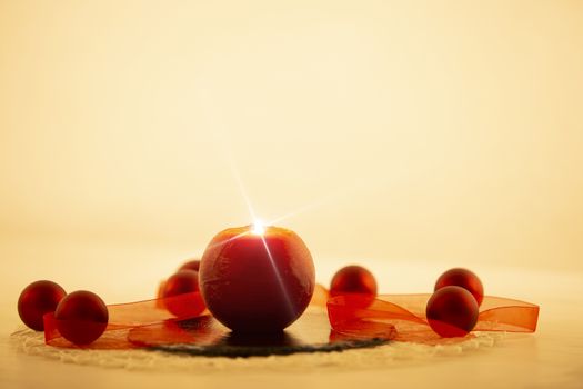 Modern Christmas copy space: close up of a red lit candle with cross screen effect on a limestone plate surrounded by red baubles and a red organza ribbon