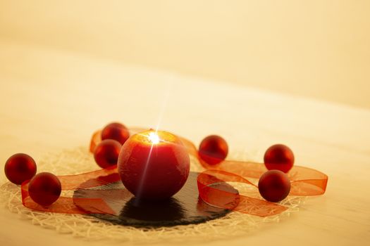 Modern Christmas copy space: close up of a red lit candle with cross screen effect on a limestone plate surrounded by red baubles and a red organza ribbon