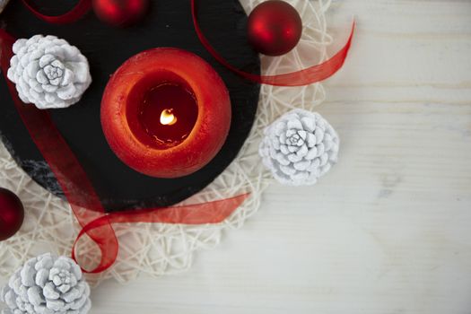 Top view of a Christmas copy space with a red organza ribbon, a black round limestone plate, white pine cones on light wooden background