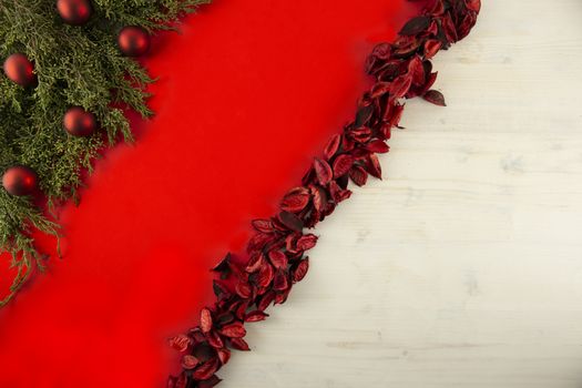 Flat lay red Christmas copy space with a diagonal red stripe on light wooden background, pine branches, red petals and red Christmas baubles