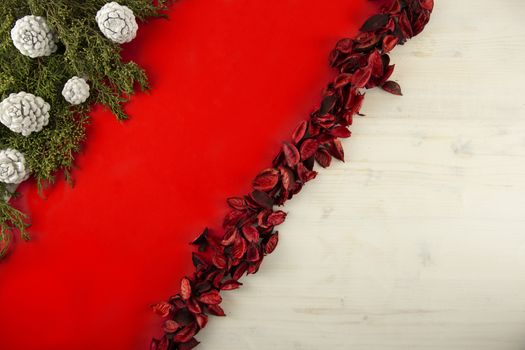 Flat lay red Christmas copy space with a diagonal red stripe on light wooden background, pine branches, white pine cones and red petals