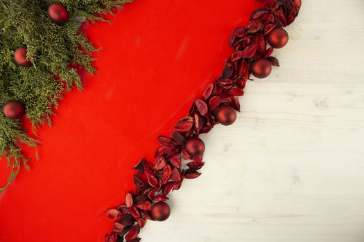 Flat lay red Christmas copy space with a diagonal red stripe on light wooden background, pine branches, red petals and red Christmas baubles