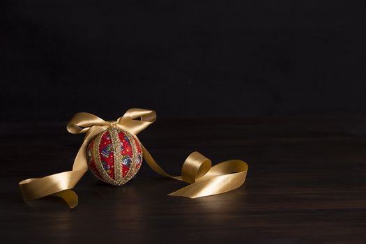 Dark wood Christmas copy space: decoupage christmas isolated ball close up with gold satin ribbon in black background