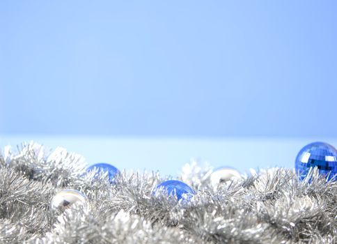 Christmas copy space with blue and silver bright baubles in silver decorative chain garland on light blue background with bokeh effect