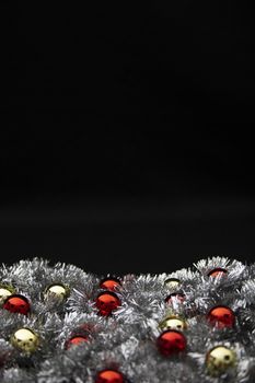 Christmas vertical copy space with red and golden bright baubles in silver decorative chain garland on black background with bokeh effect