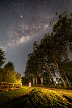 A casual dressed woman looking up in awe of the starry night sky, the Milky way rising and galactic core on a dark night in Wilton