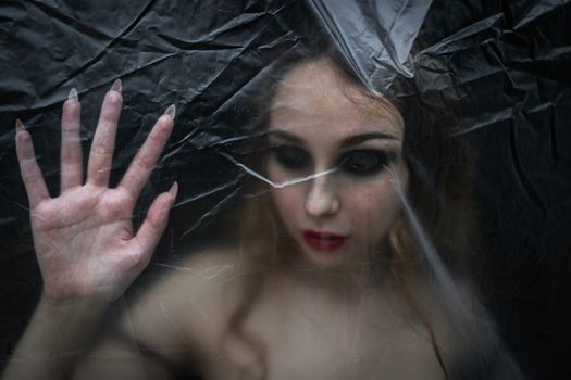 Young beauty sad woman trapped behind a plastic sheet as protection against COVID-19. Nicely fits for book cover