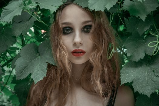 Portrait of beautiful young woman with red lips staying in front of green leaves