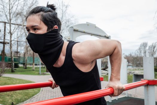 The guy is pushing up on the bars, in a black T-shirt and mask, in quarantine