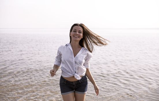 Smiling young woman enjoying her summer vacation on the beach. Beautiful female model having fun on the sea shore.