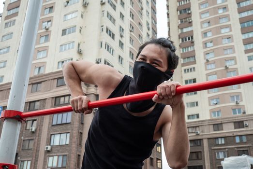 The guy is pushing up on the bars, in a black T-shirt and mask, in quarantine