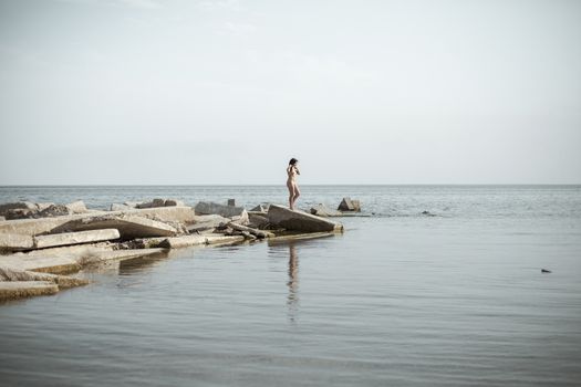 Seascape with naked swimmer girl. Overweight young woman resting in secluded place among coastal rocks