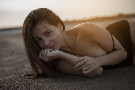 Portrait of a beautiful topless woman with wet hair and body, lying in the sand.