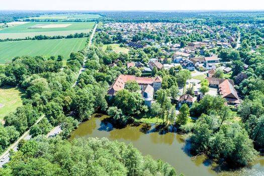 Aerial view of a German village with a small forest, a pond and a moated castle in the foreground, near Wolfsburg