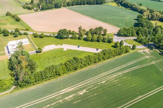 Aerial view of a small parking lot wiping rows of bushes and trees in front of the edge of an arable land, near Wolfsburg