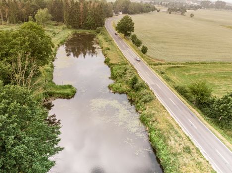 Aerial view of a small pond parallel to a country road in Saxony-Anhalt with fields and forests in the surrounding area, made with drone