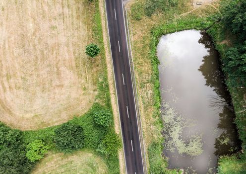 Aerial view of a small pond parallel to a country road in Saxony-Anhalt with fields and forests in the surrounding area, made with drone