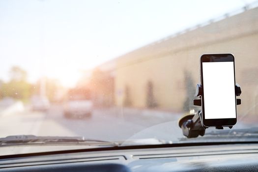 Cropped shot view The driver uses the phone while driving. Modern smart phone with round edges. Isolated screen for mockup. Car navigation display in background. 