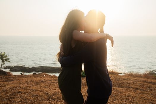 Backlit Portrait of a young romantic couple swirls in a hug against the backdrop of the sea. Anjuna Hills, Goa, India