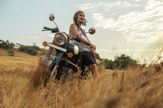 A man stands near a motorcycle in a field waiting for sunset