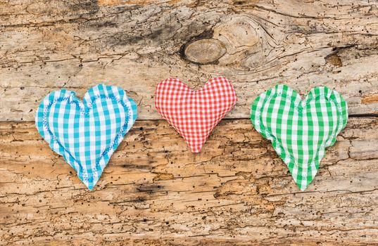 Three hearts in red, blue and green on rustic wooden background