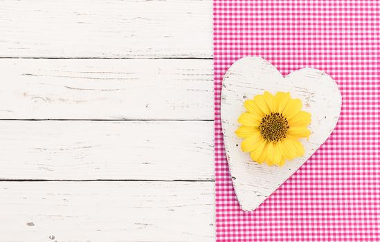 White wooden heart with yellow blossom on pink fabric and white wood background