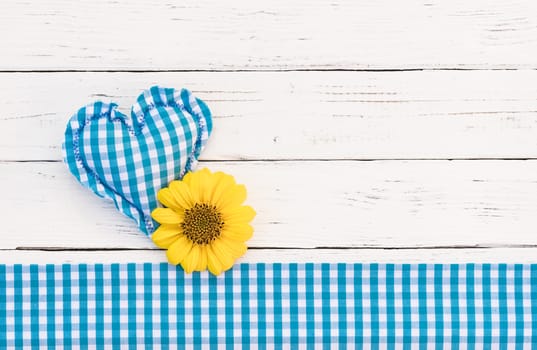 Rustic blue heart with yellow flower on white wooden background with copy space