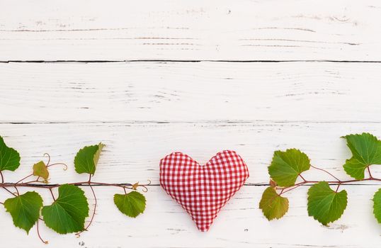 Green vine leaves with red heart on white wooden table with copy space