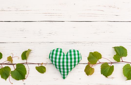 White wooden background with green vine leaves border and heart for wine celebration, event or winetasting invitation