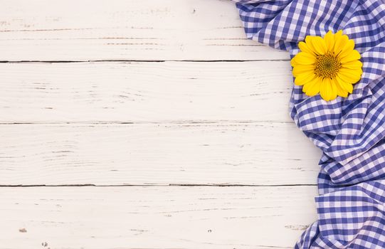 Blue tablecloth and yellow flower on white wooden table with copy space
