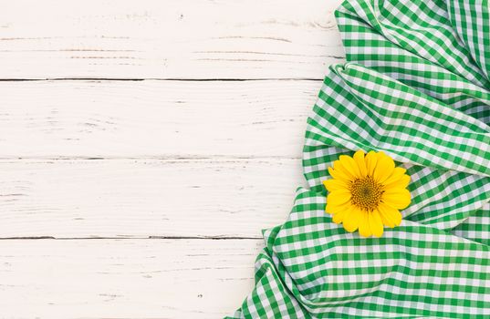 Green tablecloth and yellow flower on white wooden table with copy space