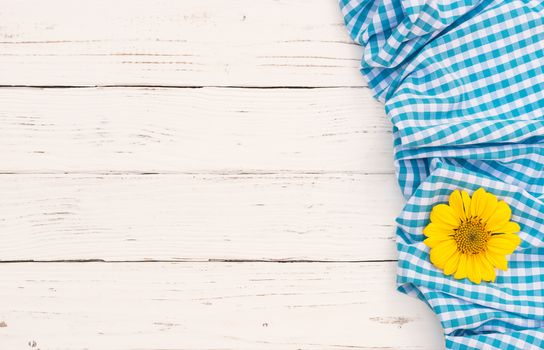 Light blue checked tablecloth and yellow flower on white wooden table with copy space