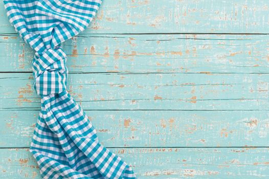 Knotted blue checked tablecloth on rustic wooden table background, top view