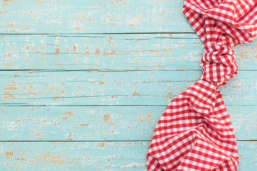 Knotted red checked tablecloth on rustic wooden table background, top view