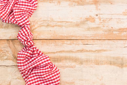 Knotted red checked tablecloth on rustic wooden table background, top view