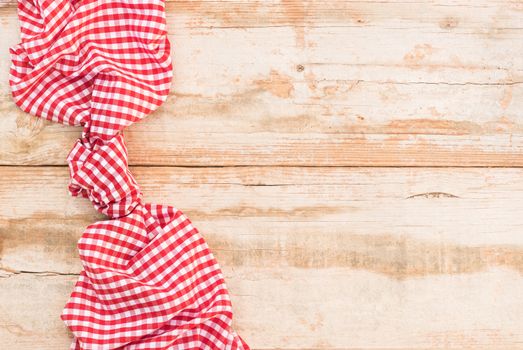 Knotted red checked tablecloth on rustic wooden table background, top view