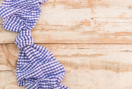 Knotted blue checked tablecloth on rustic wooden table background, top view
