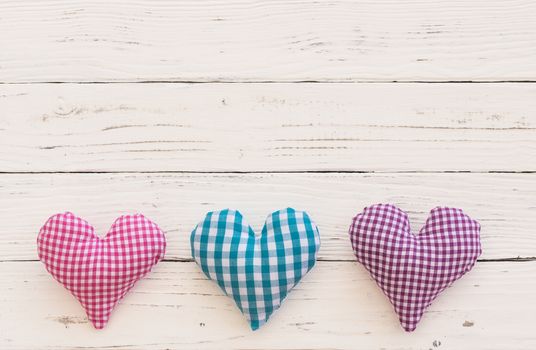 Three fabric hearts border on white wooden background with copy space