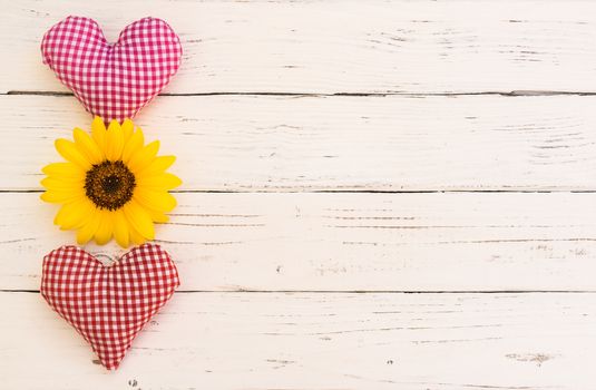 Two hearts with yellow flower on white wood with copy space