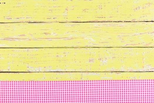 Yellow wooden table surface with pink checkered cloth, top view
