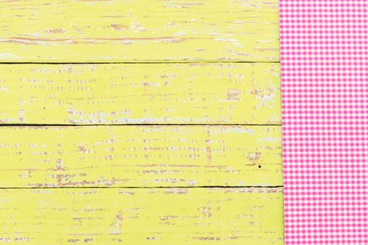Yellow wooden table background rustic texture, with pink checkered tablecloth, high angel view