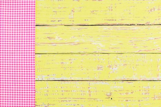 Pink checked tablecloth on rustic colored wooden table background, top view