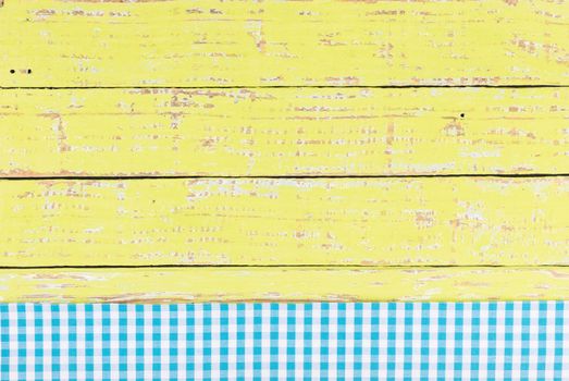 Rustic yellow wooden table surface with blue checkered cloth, top view