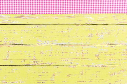 Rustic wooden table surface with pink checkered cloth, top view